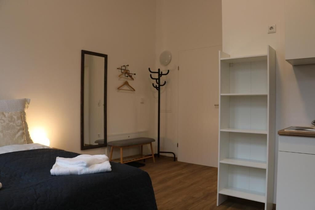 Ein Schlafzimmer mit einem Bett, einer Bank, einem Kleiderständer, einem Spiegel und einem weißen Kleiderschrank.
