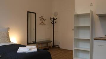 Ein Schlafzimmer mit einem Bett, einer Bank, einem Kleiderständer, einem Spiegel und einem weißen Kleiderschrank.