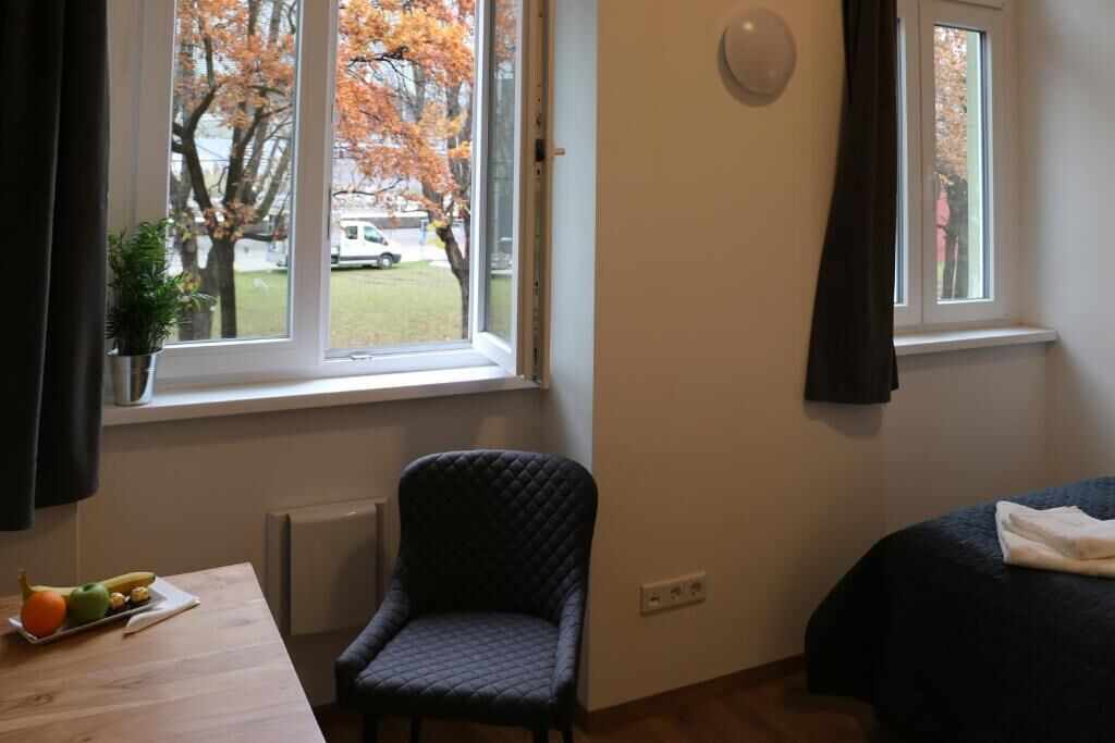 Una habitación con cama, una silla, una mesa con fruta y vistas a árboles desde la ventana.