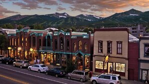 A street view of a town with historic buildings, cars parked along the road, and mountains in the background. - Grand Timber Lodge Studio, Hot Tubs, Pools & Sauna, map location is not correct (Breckenridge)