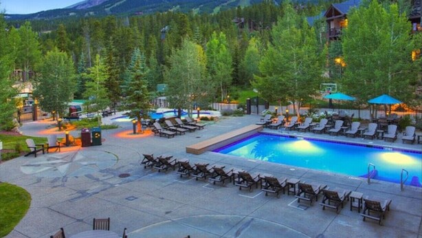 A resort pool area with lounge chairs and a swimming pool, surrounded by trees and mountains in the background. - Grand Timber Lodge Studio, Hot Tubs, Pools & Sauna, map location is not correct (Breckenridge)