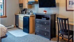 A compact kitchen with wooden cabinets, a dishwasher, a small countertop, and a flat-screen TV mounted on the wall. - Grand Timber Lodge Studio, Hot Tubs, Pools & Sauna, map location is not correct (Breckenridge)