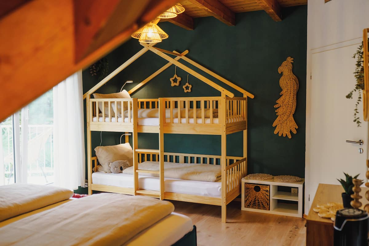 A cozy room with a bunk bed, a wooden ceiling, and a green wall with a decorative hanging.