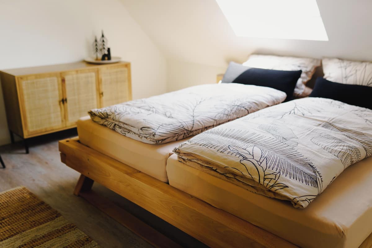 A bedroom with a wooden bed, a small cabinet, and a skylight.