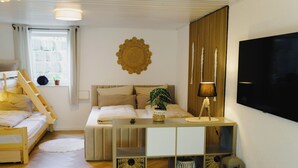 A bedroom with a bunk bed, a bedside table with a lamp, a wall-mounted TV, and a decorative wall piece. - Sohana House (Rust)