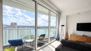Un appartement moderne doté d’un balcon, d’un canapé, d’une télévision et offrant une vue sur la ville et l’eau.