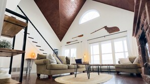 Amplia sala de estar con techo alto, vigas de madera, un gran ventanal y una chimenea acogedora.