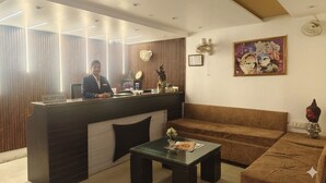 Ein Empfangsbereich mit Rezeptionistin, einem Empfangstresen mit der Aufschrift 'RECEPTION', einer Couch, einem Couchtisch und einer Wand mit einem gerahmten Bild.