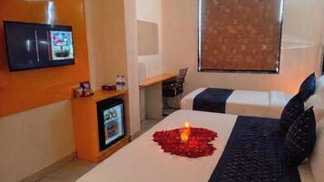 Una habitación de hotel con cama, televisión, escritorio y ventana con cortinas.