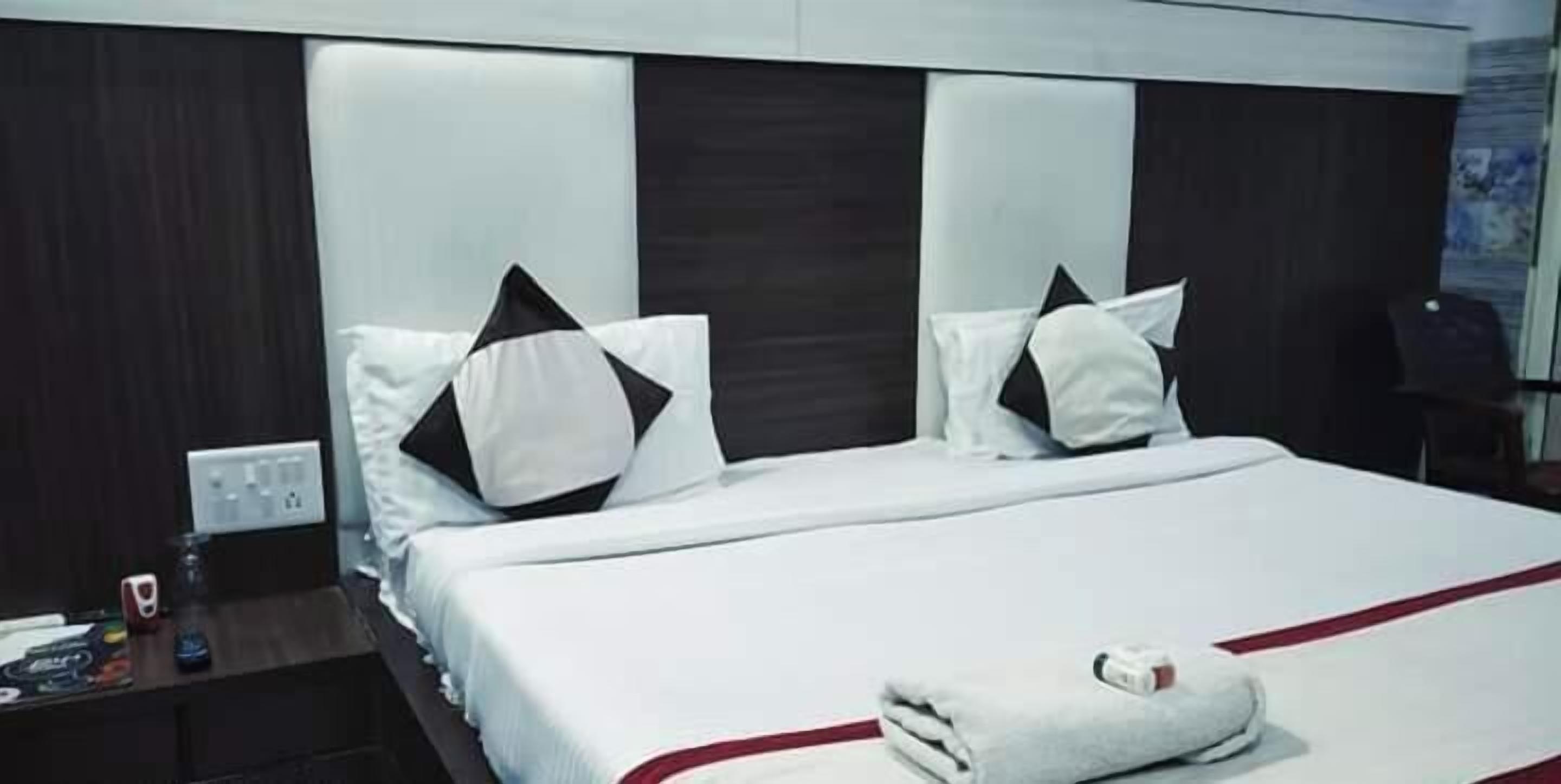 Une chambre d’hôtel avec un grand lit, deux oreillers, une table de chevet et une prise de courant fixée au mur.
