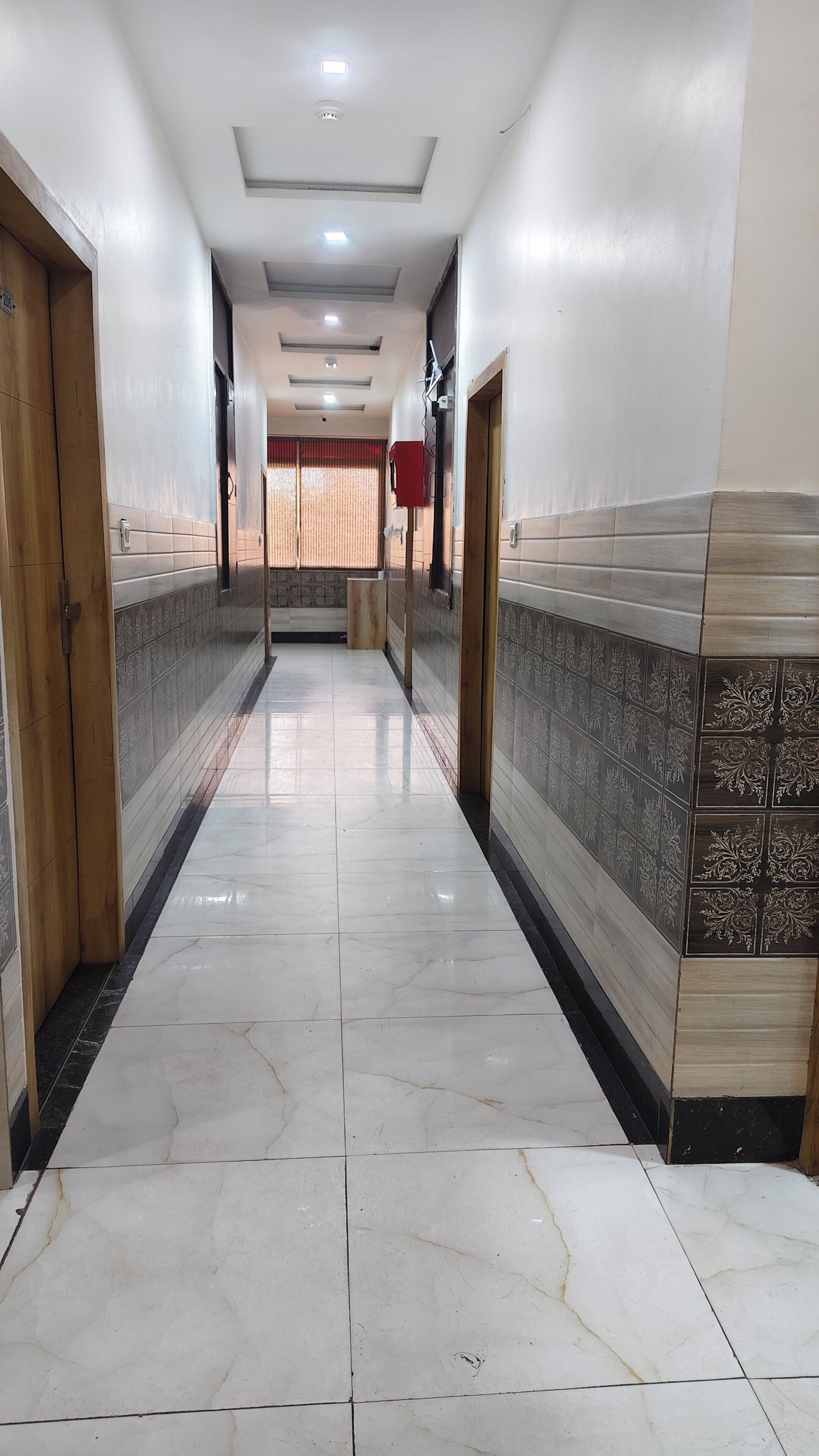 A hallway with tiled walls, a marble floor, and doors on both sides.