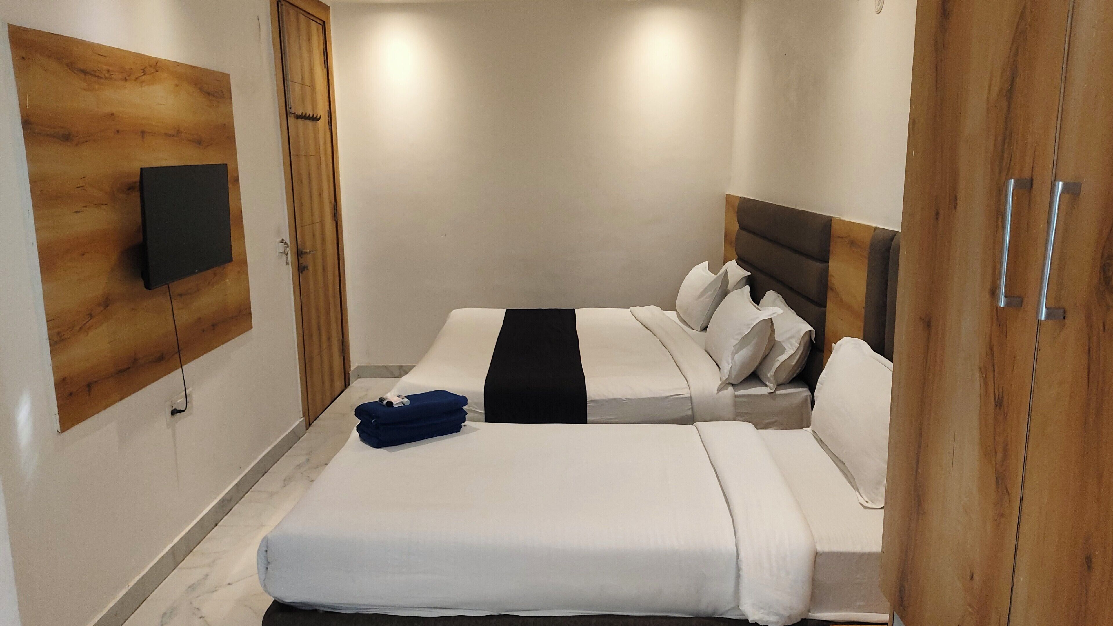 Une chambre d’hôtel avec deux lits, un téléviseur à écran plat fixé au mur, un lambris en bois et un sol en marbre.