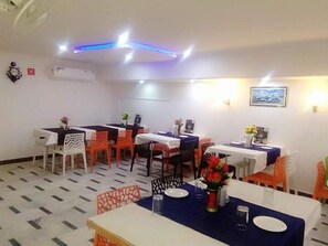 A dining area with tables and chairs, a ceiling with lights, and a wall-mounted air conditioner. - Hotel Ravi Palace Agra (Agra)