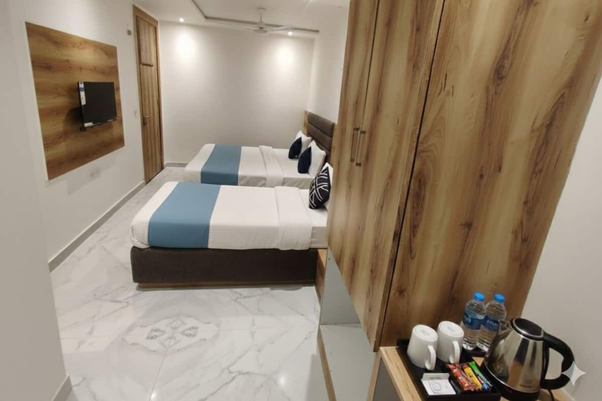 Ein modernes Hotelzimmer mit einem Holzschrank, einem Bett mit blauer und weißer Bettdecke sowie einem kleinen Nachttisch mit Wasserkocher, Tassen und Wasserflaschen.