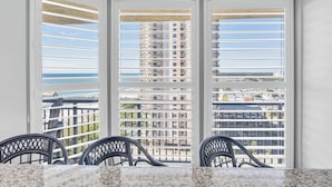 A balcony with white shutters, a view of a high-rise building, and two chairs. - Ocean View Resort Condo w Private Master Suite (Myrtle Beach)