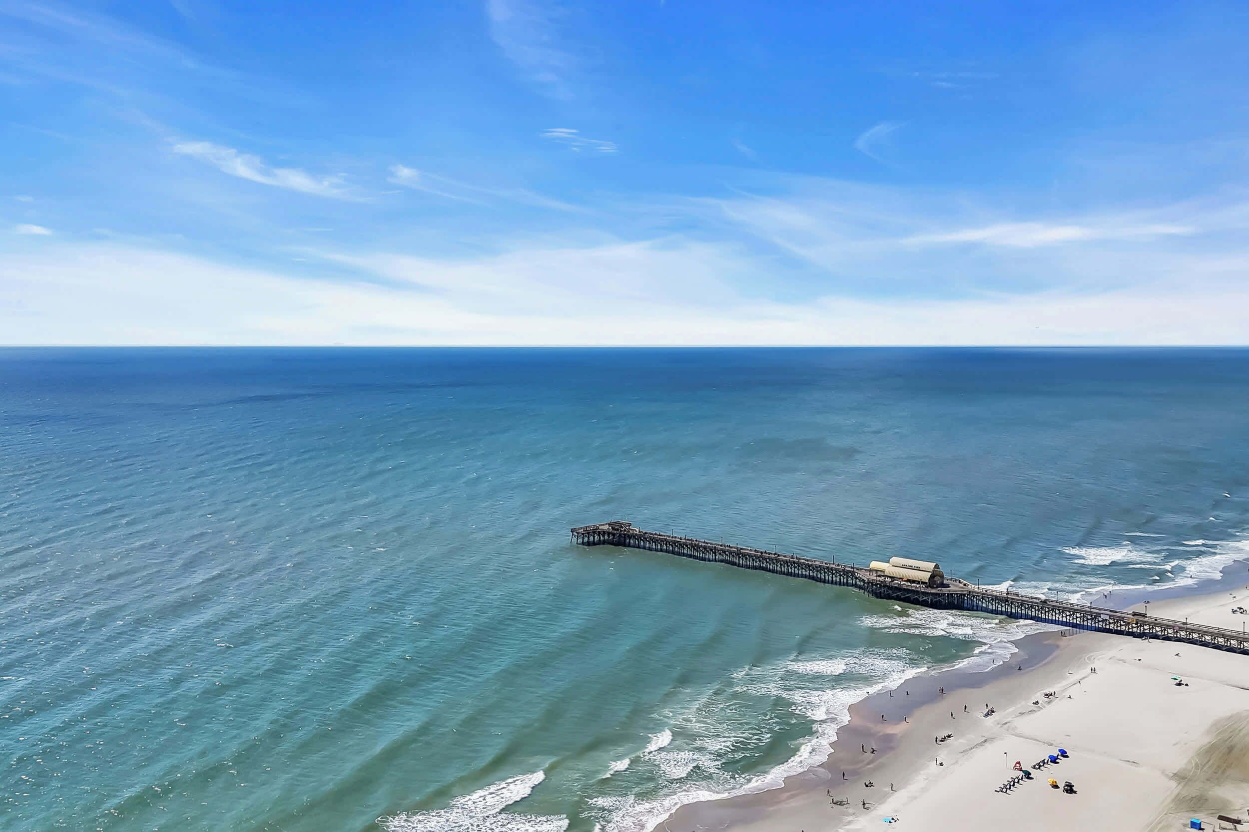 An aerial view of a beach with a long pier extending into the ocean.