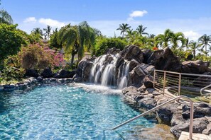 Une piscine aux eaux cristallines, agrémentée d’une cascade et entourée de rochers et de palmiers.