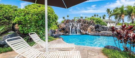 A pool area with two lounge chairs, a waterfall, and lush greenery.