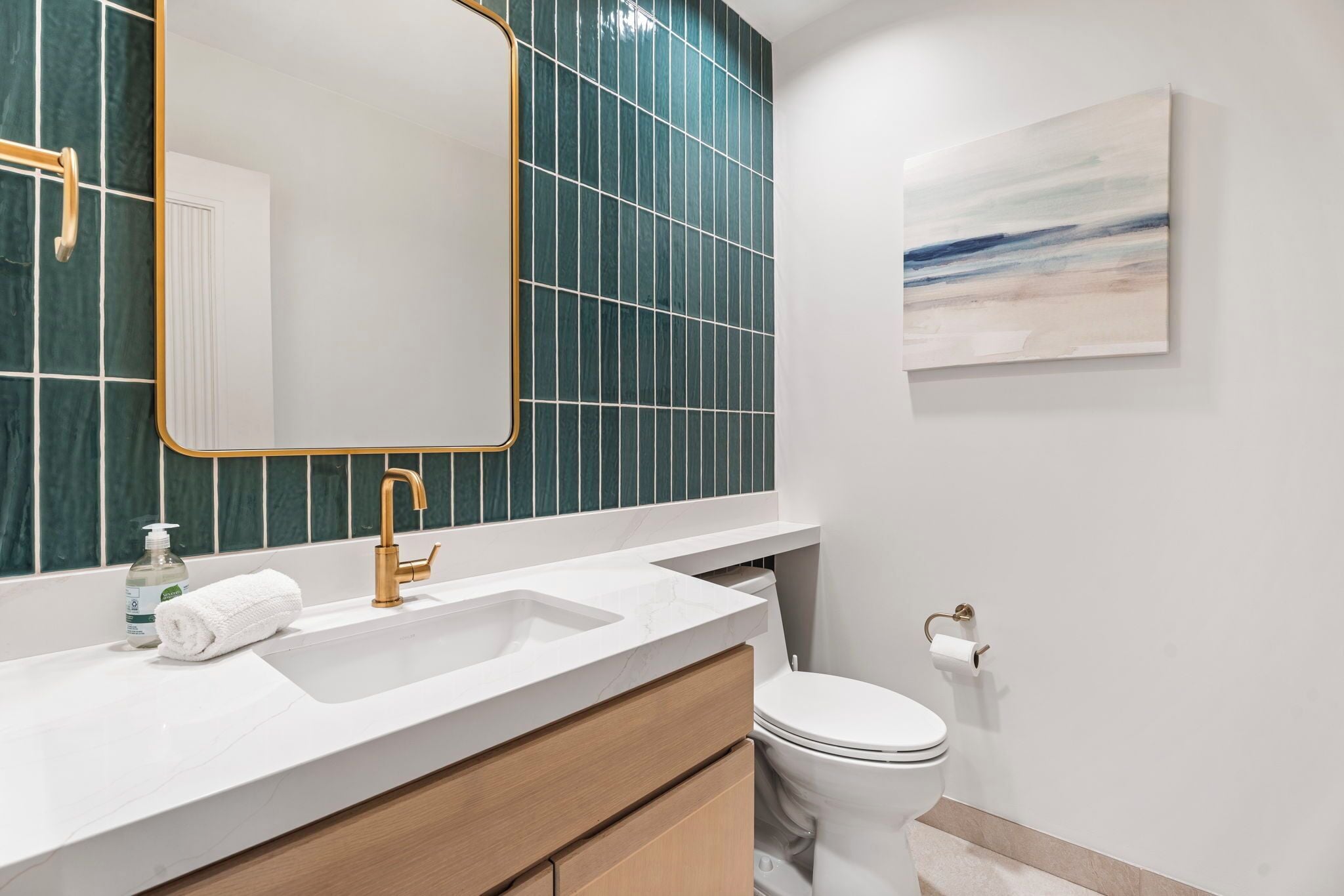 Un baño moderno con un lavabo blanco, grifo dorado y pared de azulejos verdes.