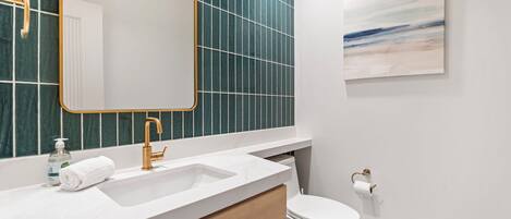 Un baño moderno con un lavabo blanco, grifo dorado y pared de azulejos verdes.