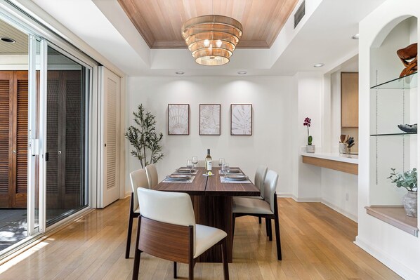 A dining area with a wooden table, chairs, and a modern chandelier. - Luxury Mauna Lani Villa Private End Unit + Resort Access - Vrkcv (Kamuela)