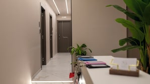 A modern hotel reception area with a marble floor, a reception desk with a plant, and a hallway leading to an elevator. - Maison D'élite (Naples)