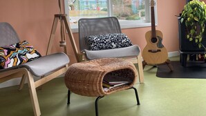 Una sala de estar acogedora con un ventanal grande, una guitarra, una planta y un sillón de mimbre.