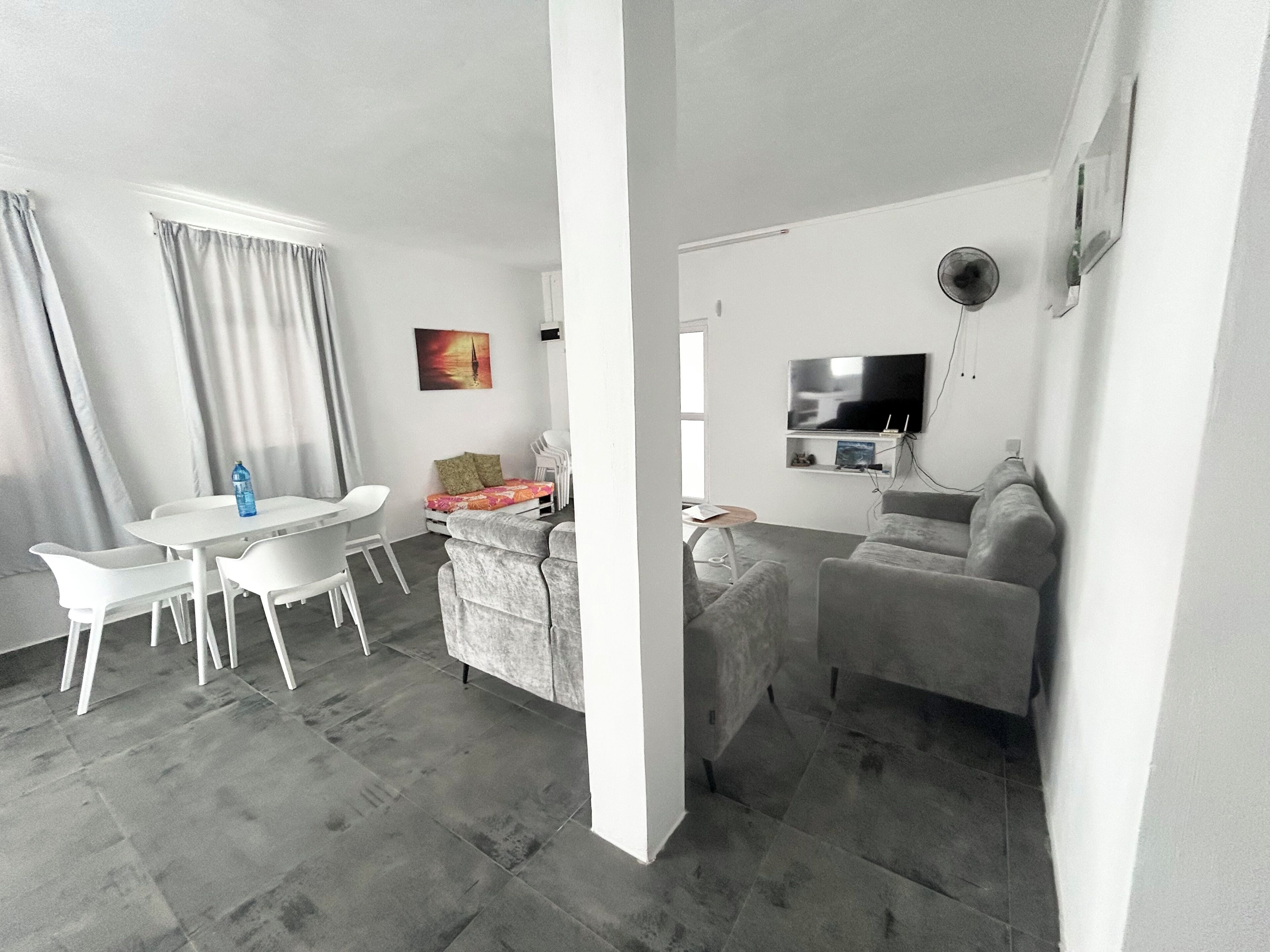 Una sala de estar moderna con un sofá, una mesa de comedor con sillas, un televisor de pantalla plana en la pared y un cuadro en la pared.