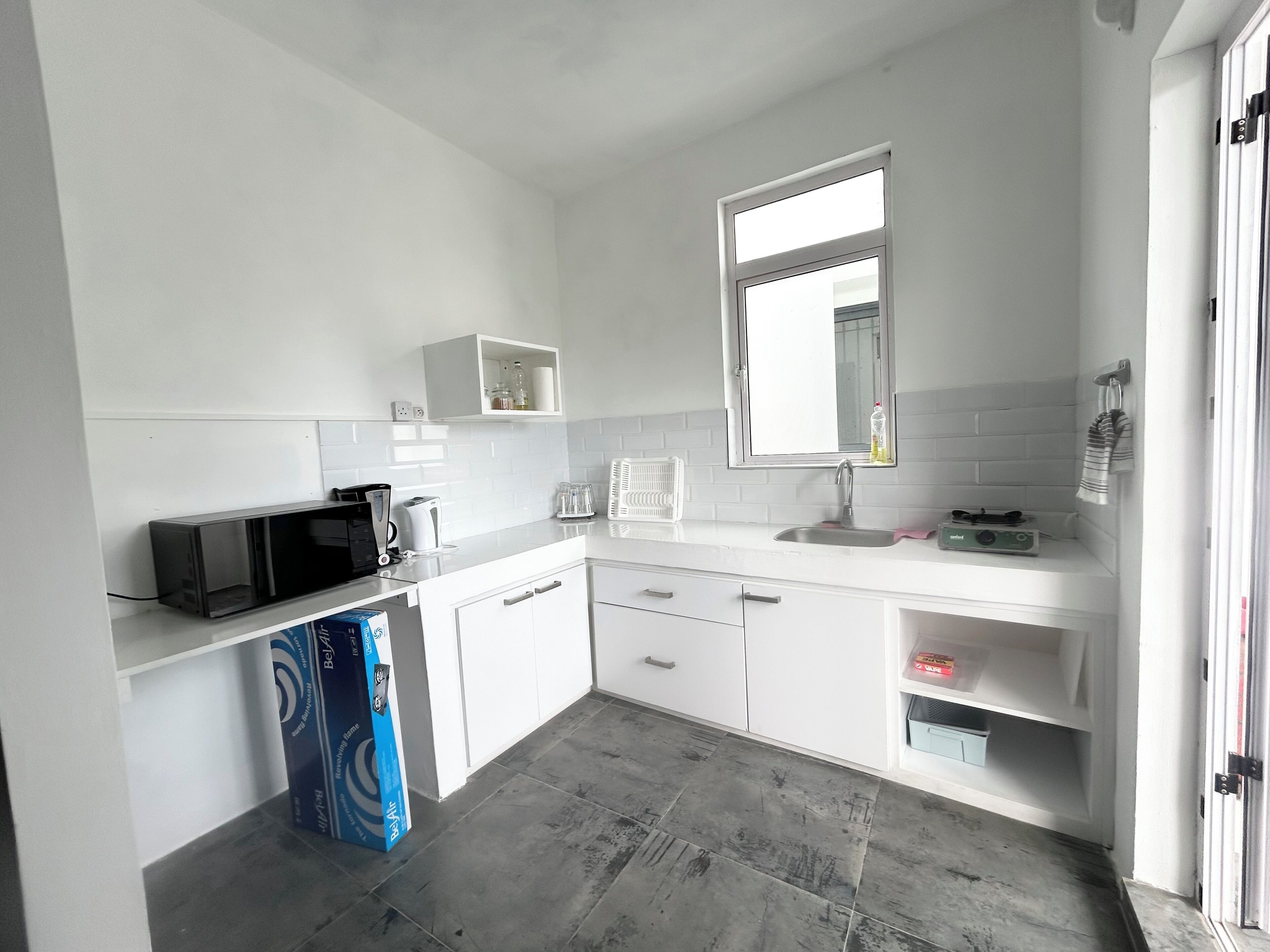 A modern kitchen with white cabinetry, a microwave, a kettle, and a sink.