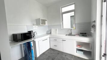 A modern kitchen with white cabinetry, a microwave, a kettle, and a sink.