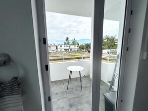 A balcony with a small table and chairs, a view of a residential area with houses and palm trees, and a clear sky.