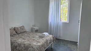 Ein Schlafzimmer mit einem Bett, einem Nachttisch, einem Fenster mit Vorhängen und einer Klimaanlage.