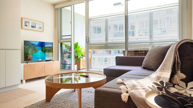 A modern living room with a glass coffee table, a sofa, and a television on a wooden cabinet. - Resort-Style 1BR Apt in Adelaide CBD | Pool & Spa (Adelaide)
