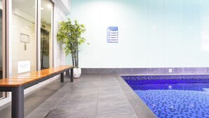 A reception area with a bench, a potted plant, and a tiled pool area. - Resort-Style 1BR Apt in Adelaide CBD | Pool & Spa (Adelaide)
