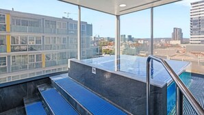 A modern indoor pool area with a glass wall offering a city view. - Resort-Style 1BR Apt in Adelaide CBD | Pool & Spa (Adelaide)