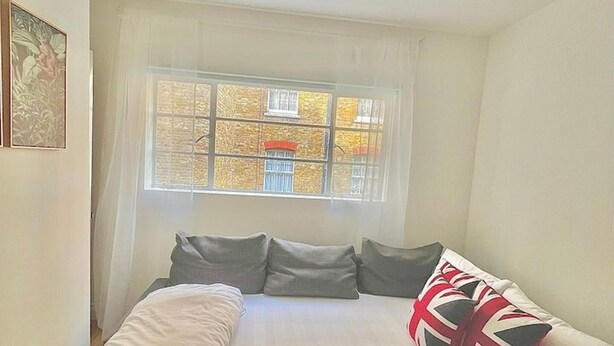 A bedroom with a bed, pillows, a window, and a painting on the wall. - 3 Bedroom Flat in Kings Cross (London)