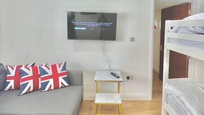 A modern room with a grey sofa, a television mounted on the wall, a small white table, and a bunk bed. - 3 Bedroom Flat in Kings Cross (London)