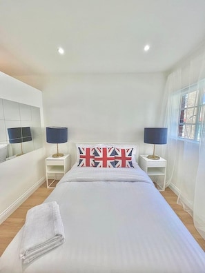 Una camera da letto moderna con un letto grande, due comodini con lampade, una televisione sulla parete sinistra e una finestra sulla destra.