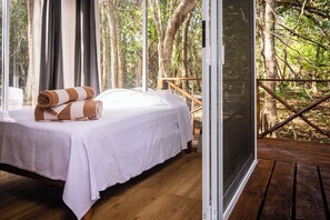 A bed with a white sheet and a rolled towel, a wooden floor, and a view of trees through a window. - When Dream Come true (Akumal)