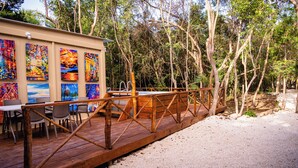 Une terrasse en bois avec une rambarde en métal, entourée d’arbres et d’un bâtiment dont les murs sont ornés d’œuvres d’art colorées.