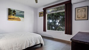 Ein Schlafzimmer mit einem Bett, einem Fenster mit Vorhängen, einem Strandbild und einer gerahmten Grafik an der Wand.
