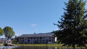 A hotel with a large building, a lake in front, and a tree to the right. - Nice studio for 2 or more people with view of small lake (Chauffailles)