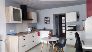 A compact kitchen with modern appliances, a dining area with a small table and chairs, and a visible door leading to another room. - Nice studio for 2 or more people with view of small lake (Chauffailles)