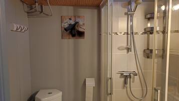 A bathroom with a glass-enclosed shower, a toilet, and a towel dispenser.
