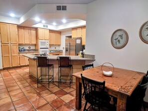 A kitchen with wooden cabinets, a central island with bar stools, a dining table with chairs, and a refrigerator. - Authentic Desert Vibes 3-bedroom house with pool & AC in charming Cave Creek (Cave Creek)