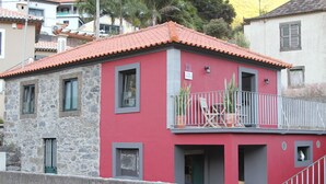 Un edificio a due piani con facciata rossa, una parte inferiore in pietra e un balcone con ringhiera.