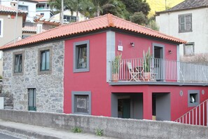 Ein zweigeschossiges Gebäude mit roter Fassade, einem Steinsockel und einem Balkon mit Geländer.