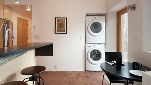 A compact kitchen with a washing machine, a dining table, and a bar stool.