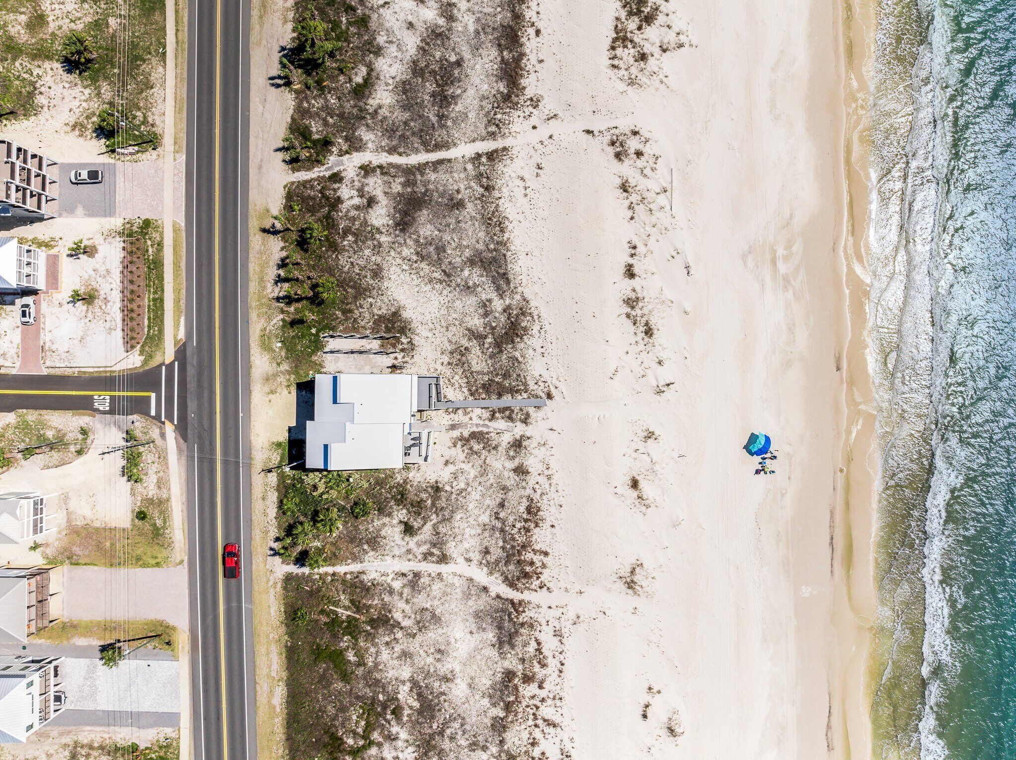 Luchtbeeld van een strand met een weg, een gebouw en een strandparasol.
