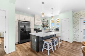 A modern kitchen with a large island, white cabinetry, and a stainless steel refrigerator. - Steps to the Sand – Beach Gear, Boat Parking (Port St Joe)